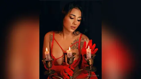 Woman in red lingerie with tattoos posing by glowing candles in a moody, romantic setting.