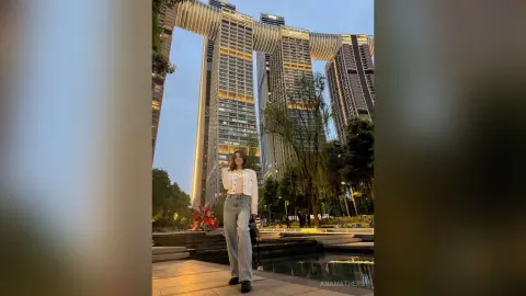 Young woman in white blouse and jeans standing before modern skyscrapers at twilight.