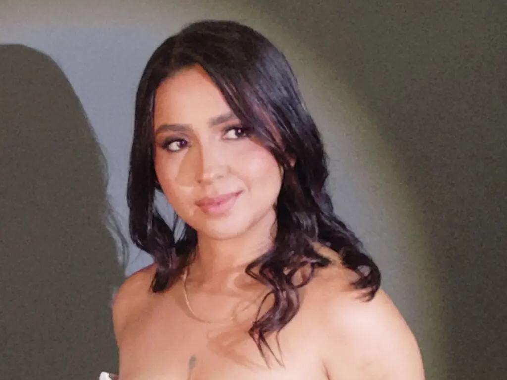 Smiling woman with wavy dark hair wearing a strapless top in soft, moody lighting.