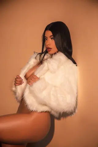 Glamorous woman in a white faux fur coat posing against a warm beige background for a luxury fashion look.