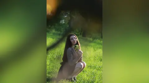 Dreamy portrait of a woman in a brown dress holding wildflowers in a lush green meadow at sunset.