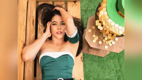 JessieLiu lies on a wooden surface wearing a dark green off-the-shoulder top, running her hands through her long dark hair.