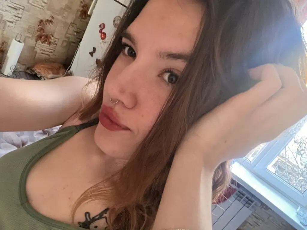Close-up portrait of a young woman with long brown hair wearing a green tank top in a bright indoor setting.