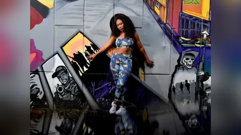 Stylish woman in blue patterned lounge set posing confidently against a vibrant urban street art mural.