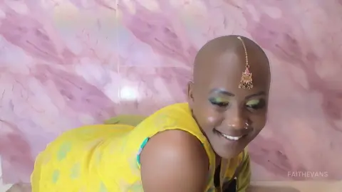 Smiling woman in a bright yellow outfit with traditional gold head jewelry against a pink marble background.