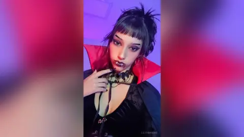 Gothic woman in black vampire costume with red collar and lace choker posing in moody purple lighting.