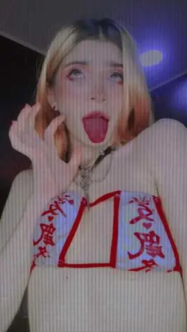 Blonde woman in a white and red patterned crop top making a playful expression in moody lighting.