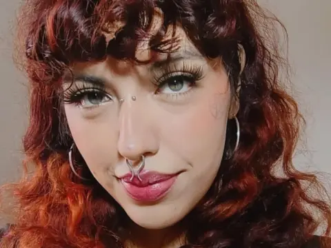 Close-up portrait of a woman with wavy red hair, nose ring, and long eyelashes in a soft, natural mood.