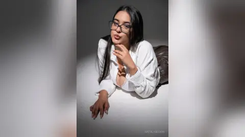 NatalyBloom wearing glasses and an open white shirt while lying on her stomach.