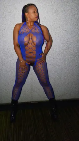 Confident woman in a blue mesh cutout bodysuit posing against a textured wall.