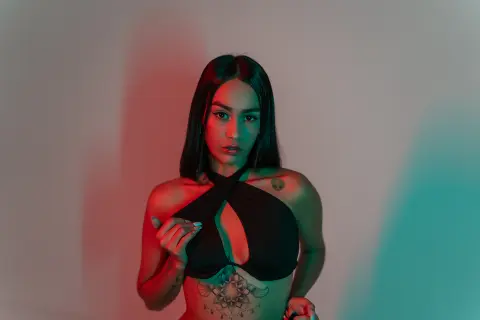 Young woman in a black halter top posing under moody red and teal studio lighting.