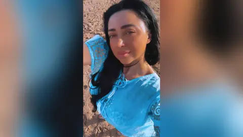 Smiling woman in a blue bohemian blouse enjoying a sunny day at the beach.