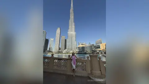 Stylish woman in a white summer outfit standing by a waterfront with the Burj Khalifa skyscraper in Dubai.