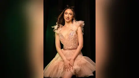 Elegant woman in a sparkling pink feathered gown posing glamorously against a dark studio background.