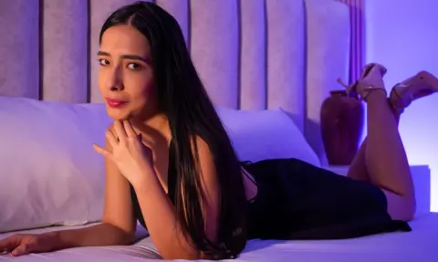 Elegant woman in a black dress relaxing on a white bed with moody purple lighting.