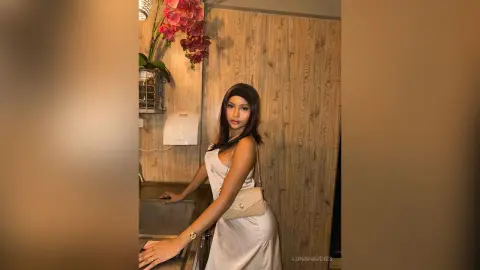 Elegant woman in a white satin slip dress posing in a modern kitchen with pink orchids.