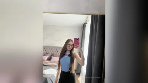 MilanaVolkova takes a mirror selfie wearing a light blue tank top and black skirt, showing off her long straight hair and glasses in a bedroom setting.