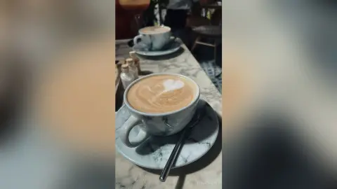 Latte art heart in a ceramic cup on a marble cafe table during a cozy morning coffee break.