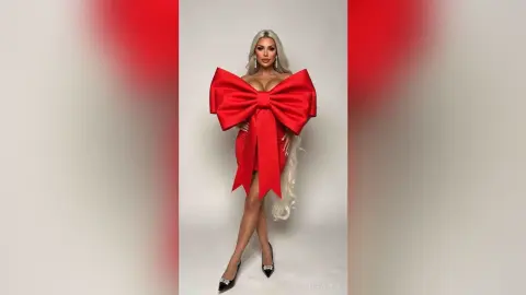 Glamorous blonde woman in a bold red bow dress posing against a white studio background.