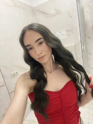 Young woman with long wavy hair wearing a red strapless top in a modern marble bathroom.