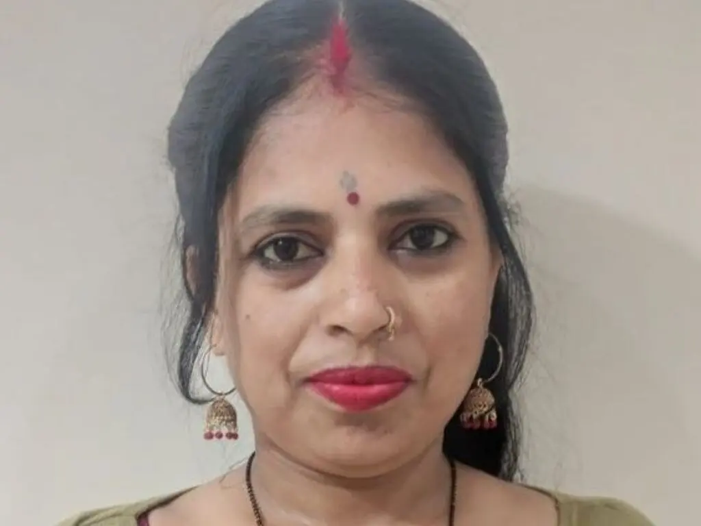Portrait of a smiling Indian woman with traditional bindi and gold earrings in a neutral indoor setting.