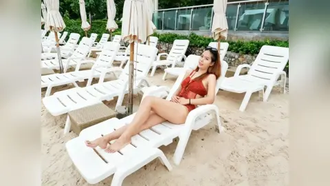 Relaxed woman in a red swimsuit lounging on a white beach chair under sunny resort umbrellas.