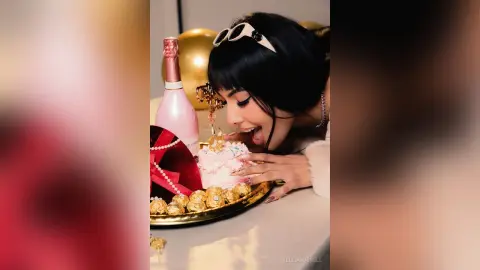 Glamorous woman in white outfit celebrating with pink champagne and a festive cake in a joyful mood.