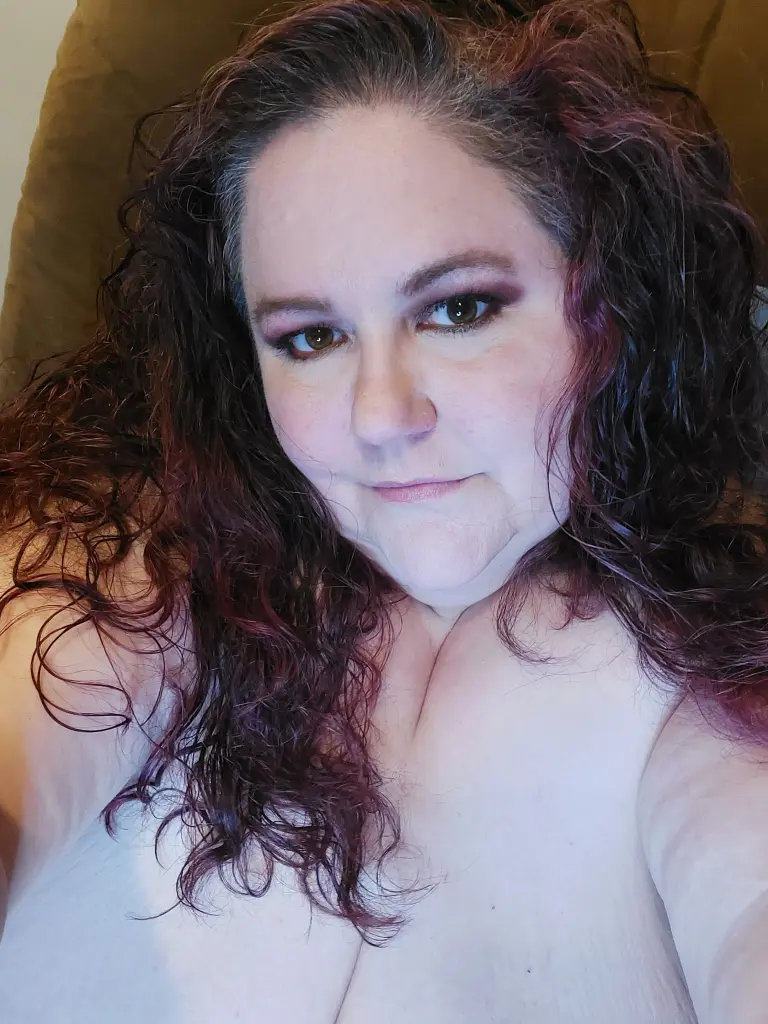 BigBeautifulWitch poses with long brown hair and glasses, wearing a blue patterned top while looking directly at the camera.