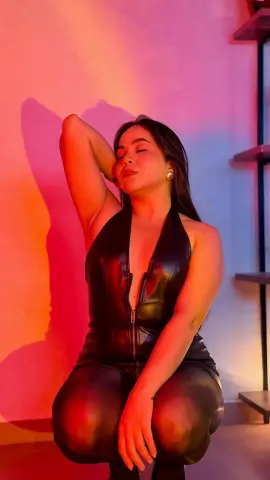 Woman in a black leather jumpsuit posing against a warm red and blue studio background.