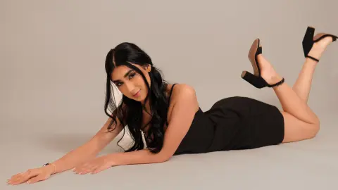 Young woman in a black dress lying on a grey studio floor posing with a playful mood.