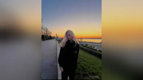 Young woman in a black outfit standing on a seaside walkway during a golden sunset mood.