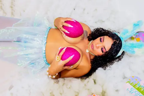 Curvy woman in a shimmering pastel fairy outfit lying on white fluffy clouds for a dreamy fantasy photoshoot.