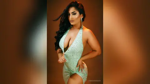 Glamorous woman in a sparkling mint green halter dress posing against a warm studio background.