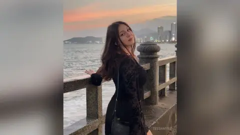 Young woman in a black long-sleeve top leaning on a stone pier overlooking the ocean at sunset.