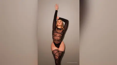 Elegant woman in a black sheer bodysuit posing against a neutral studio background with a sophisticated mood.