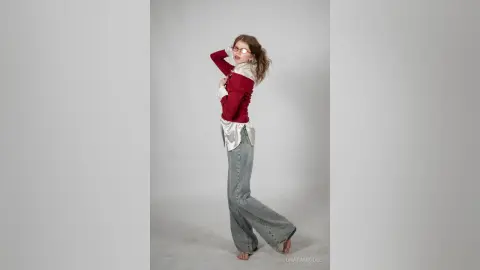 Young woman in a red long-sleeve shirt and wide-leg denim jeans posing against a white studio background.