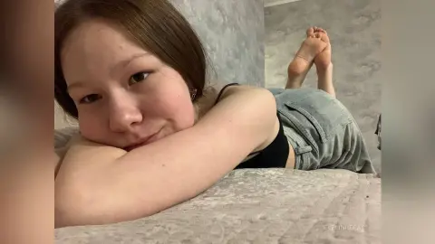 Young woman in denim shorts relaxing on a textured bed in a cozy, casual indoor setting.
