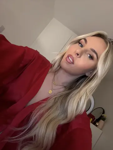 roseangelap poses with long blonde hair and a red robe, wearing gold necklaces and looking at the camera with a pouty mouth.