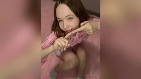 Young woman in a pink crochet top smiling while sitting on a soft pink fuzzy rug in a cozy indoor setting.
