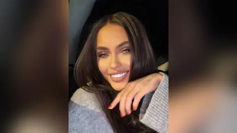Smiling brunette woman in a cozy grey sweater sitting in a car at night.
