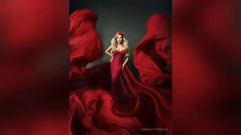 Elegant blonde woman in a flowing red gown amidst dramatic swirling crimson fabric in a moody studio setting.