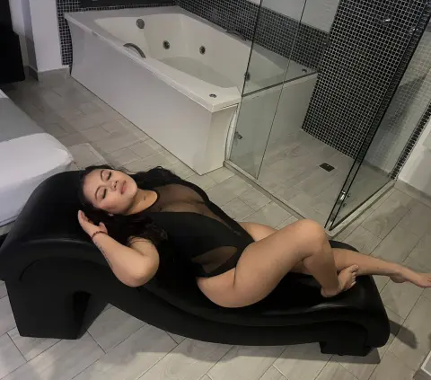Young woman in a black bodysuit relaxing on a black lounge chair in a modern bathroom setting.
