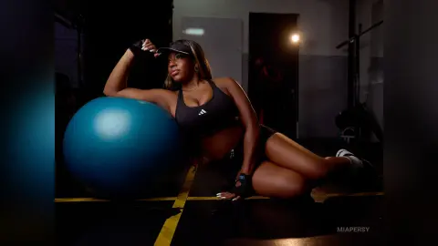 Fit woman in black gym wear relaxing on a blue exercise ball in a moody, dimly lit fitness studio.