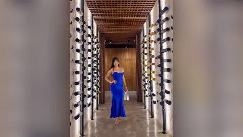 Elegant woman in a sleek blue evening gown standing in a modern luxury wine cellar.
