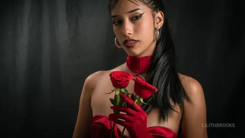 Elegant woman in a red velvet dress and gloves holding roses against a dark moody background.