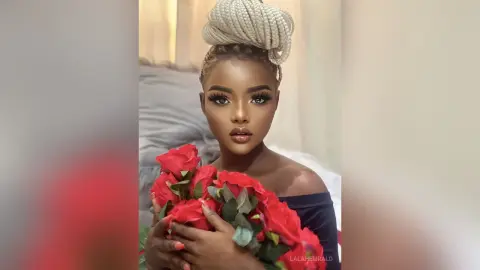 Beautiful woman with braided updo holding a bouquet of red roses in a soft, romantic indoor setting.