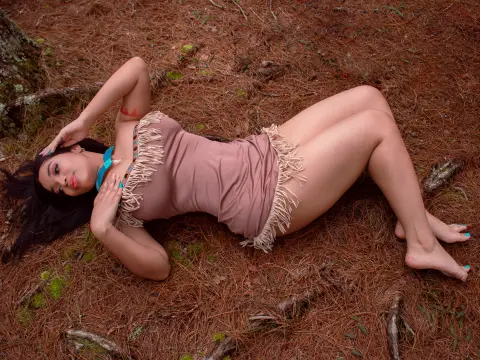Woman in a brown fringe bodysuit relaxing on a bed of pine needles in a forest setting.