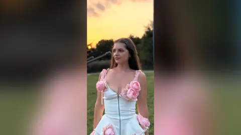 Young woman in a white floral corset dress posing outdoors during a golden hour sunset.