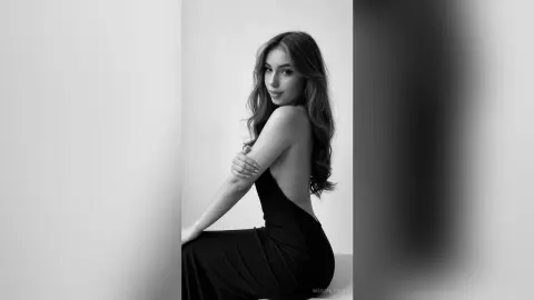 MeganLewit poses in a black dress, looking over her shoulder with her long wavy hair flowing down her back.