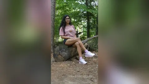 Young woman in pink t-shirt and white sneakers relaxing on a log in a lush green forest.